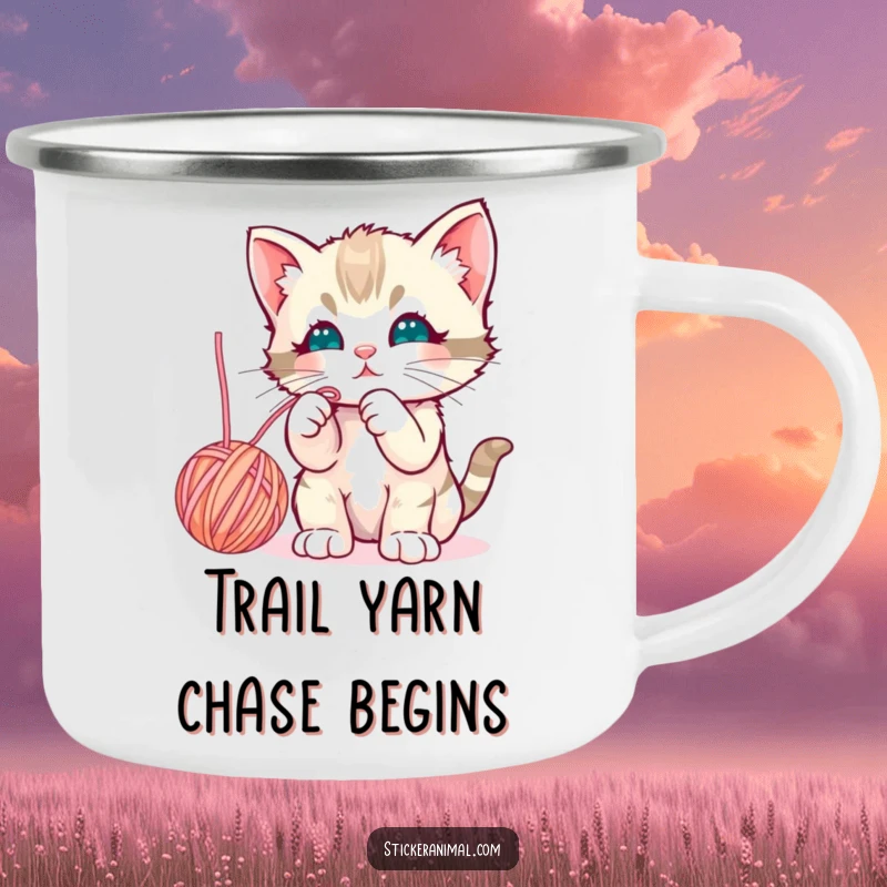 Funny curious kitten batting playfully at a dangling yarn ball on a durable enamel camping mug for outdoor beverages.
