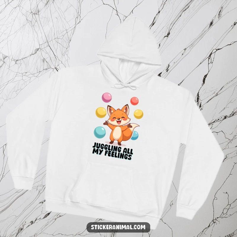 Funny hoodie depicting a grinning fox masterfully juggling large, colorful balls, perfect for staying warm and expressing playful energy.